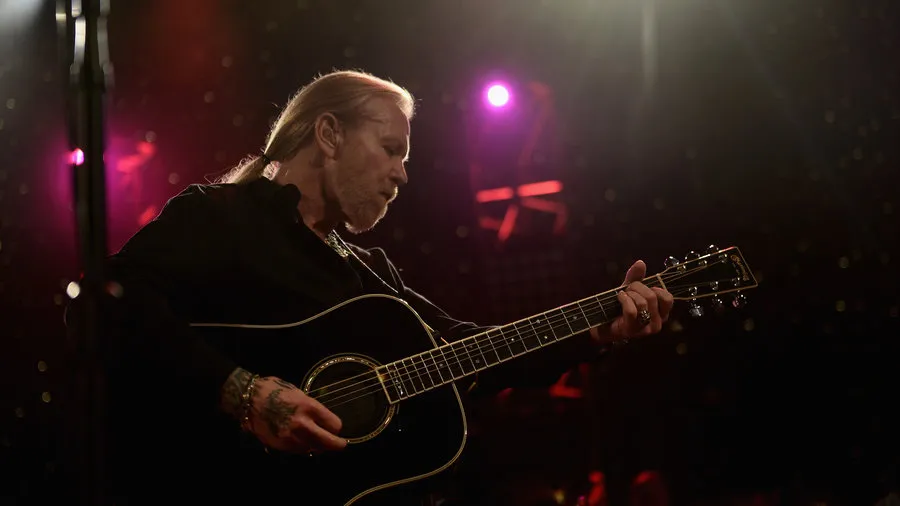Gregg Allman performing live on stage with his guitar, showcasing his Southern rock blues style during a concert